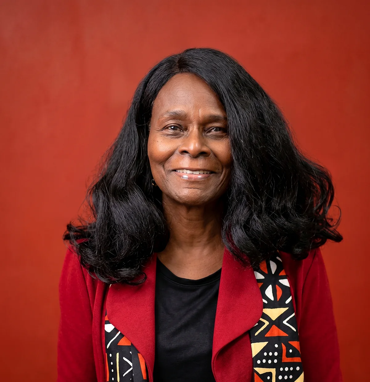 Olinga Yarber-Alexander smiling, wearing a red jacket with a patterned scarf
